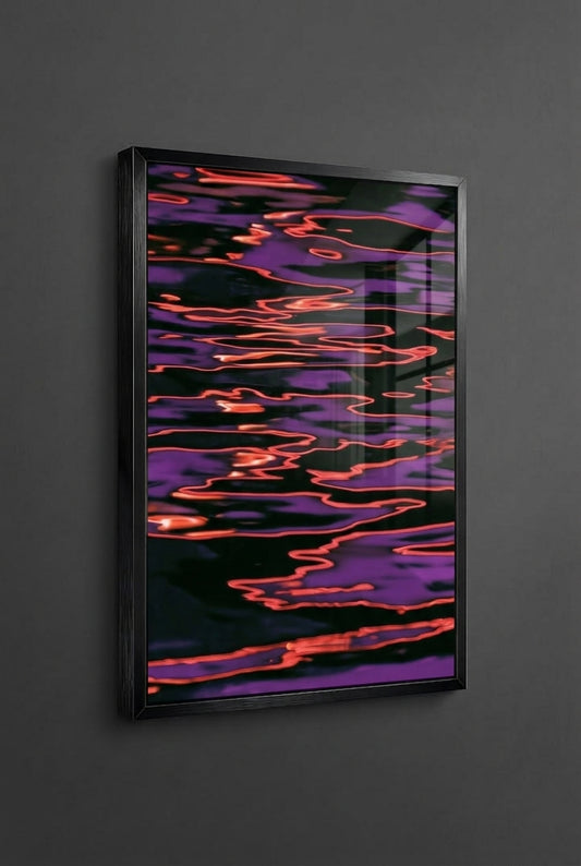 A framed abstract art print featuring a black background with flowing purple and orange-red light-like patterns, mounted on a dark gray wall.