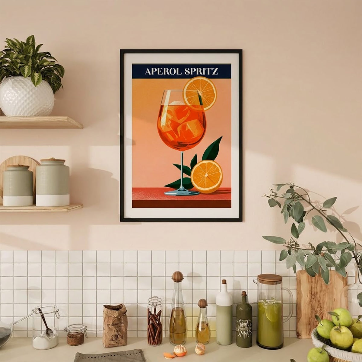 A framed travel-style poster of an Aperol Spritz cocktail hangs on a beige wall in a kitchen setting. The poster features an orange drink in a glass with orange slices and green leaves, with the text 'APEROL SPRITZ' at the top.