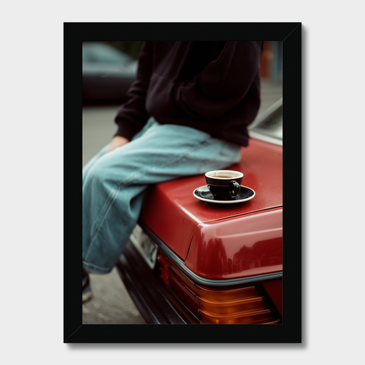 Person sitting on a red car with a coffee cup on the hood