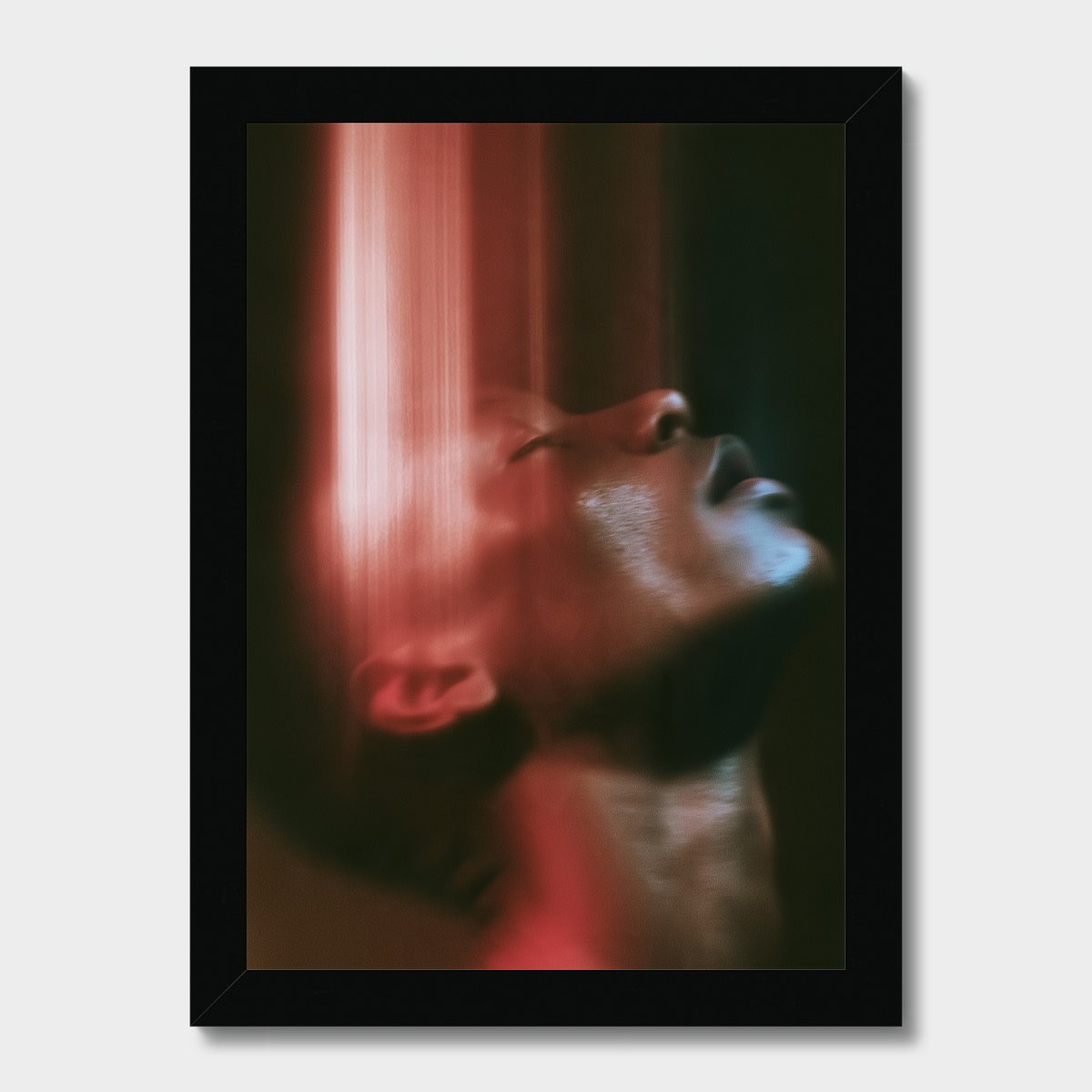A framed art print featuring a close-up portrait of a person's face in profile, illuminated by dramatic red and pink light against a dark background, set in a black frame.