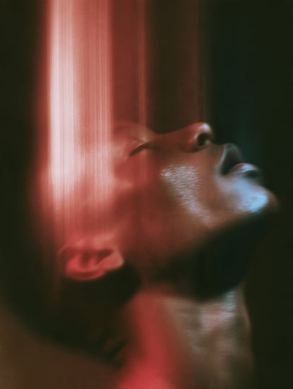 A close-up portrait of a person's face tilted upward, captured with dramatic motion blur and strong red lighting against a dark background.