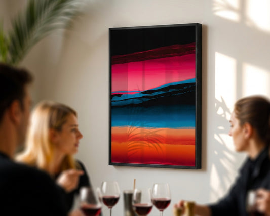 A framed abstract landscape art print with vibrant pink, blue, and orange sunset-like bands hanging on a light beige wall in a dining room setting, with blurred people seated at a table in the foreground.