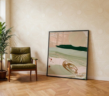 A large framed abstract art print with soft beige, sage green, and dark teal brushstrokes leans against a patterned wallpaper wall in a modern room next to an olive green leather armchair and a potted plant.