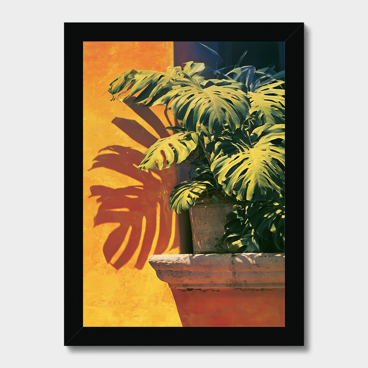 Framed wall art featuring a potted monstera plant in a terracotta pot against a warm yellow wall with a cast shadow, shown in a black frame on a light gray background.