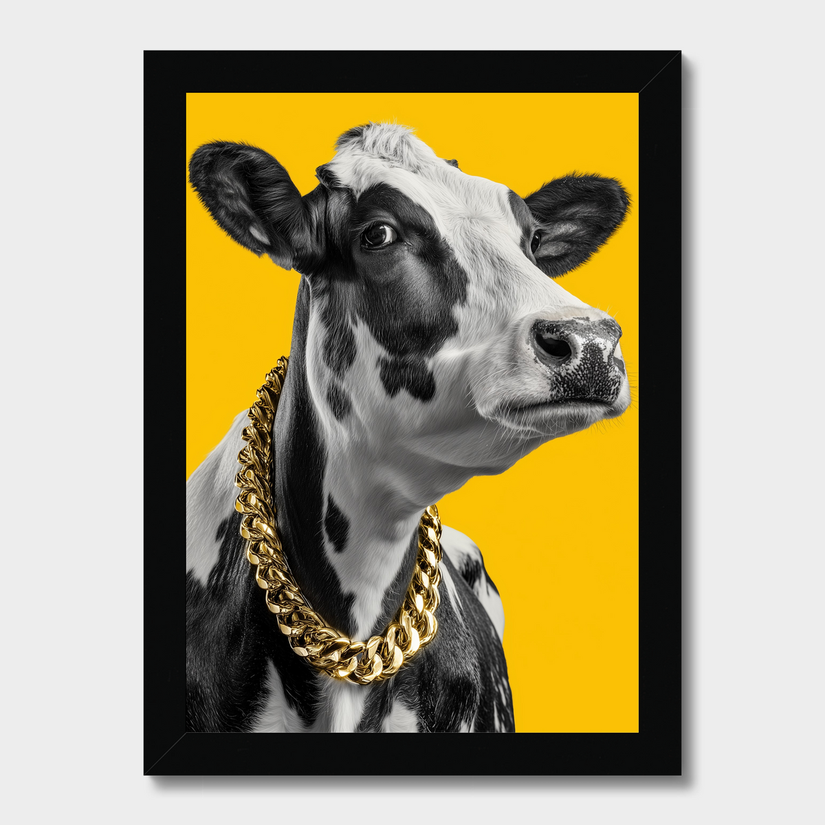 Framed wall art featuring a black-and-white cow portrait with a large gold chain necklace against a bright yellow background, shown in a black frame on a light gray wall.