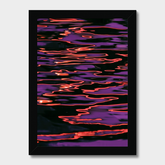 A framed abstract art print depicting shimmering purple and orange reflections on a dark water surface, presented in a black frame against a light gray background.