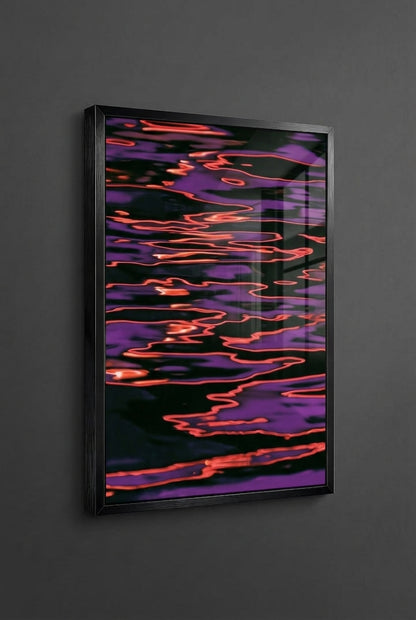 A framed abstract art print featuring a black background with flowing purple and orange-red light-like patterns, mounted on a dark gray wall.