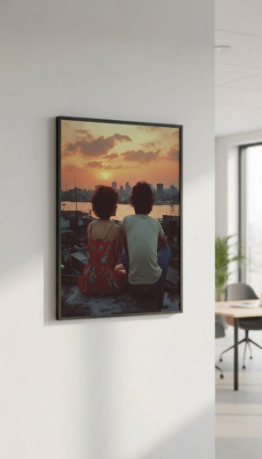 A framed vertical art print depicting a couple sitting by a waterfront at sunset, displayed on a white wall in a modern office setting.