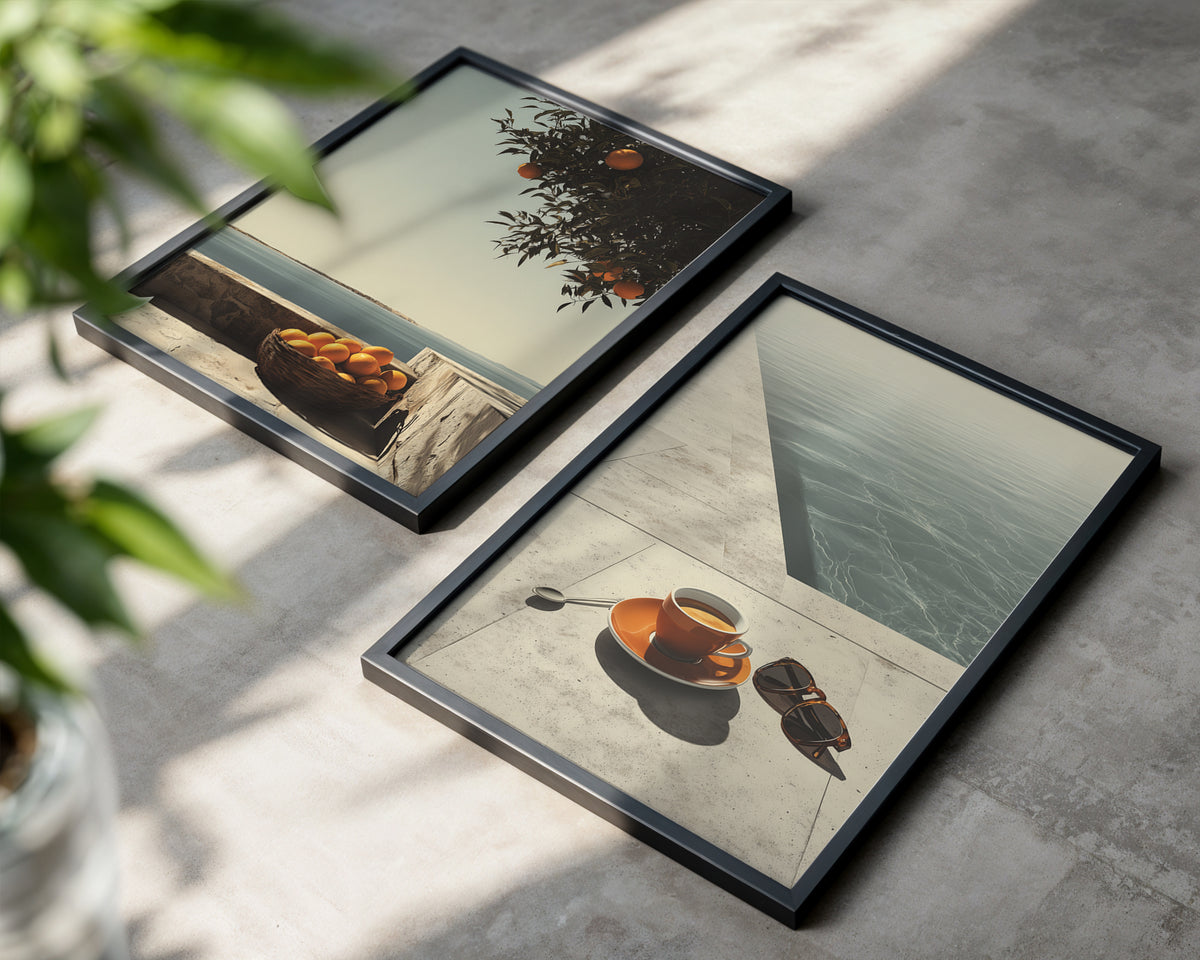 Two framed square art prints with black frames displayed on a concrete surface. The left print shows a beach scene with a basket of oranges under tree branches.