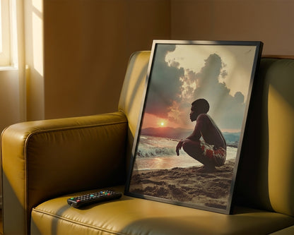 A framed art print depicting a man crouching on a beach at sunset, leaning against a yellow leather armchair in a warmly lit room.