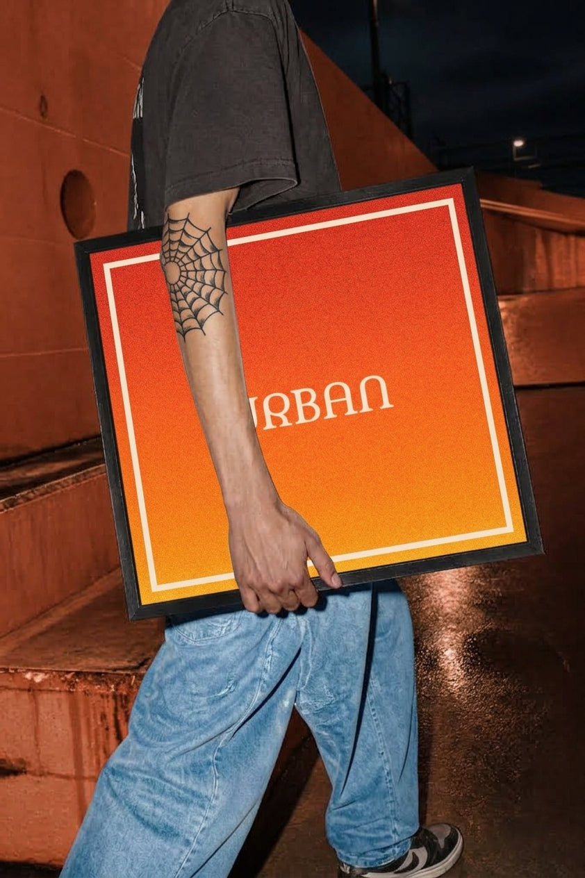 A person in a black t-shirt and blue jeans carries a large square framed sign with a red-to-orange gradient background and the word 'URBAN' in white. The scene is set in a dimly lit industrial environment at night.