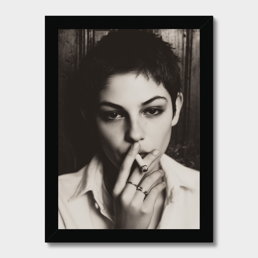 A framed black and white portrait print of a woman with short hair, wearing rings, set against a dark wood background, shown in a black frame on a light gray background.